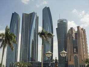 Modern skyscrapers and palm trees, with decorative lanterns in the foreground, under blue sky,