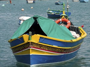 A colourful fishing boat with green fabric cover and lifebuoy at anchor, many colourful fishing