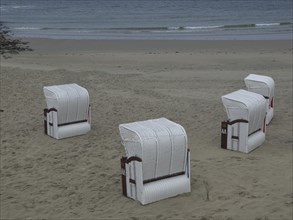 Four white beach chairs on an empty beach with calm sea in the background, beach chairs and beach
