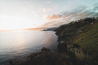 The sun sets over the sea and colours the sky over the calm coastline. Madeira Portugal