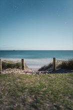 Starry night sky over a quiet beach and sea, demarcated by wooden posts and rope