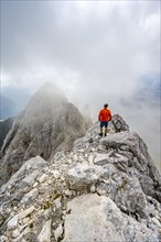 Mountaineer on a rocky narrow summit ridge, cloudy mountain peak, summit of the Great Kinigat,