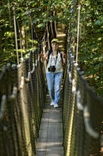 Sporty woman, tourist with camera in treetop path, suspension bridges, ropes, nets, beech forest,