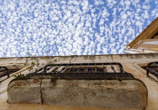 Old rusty, overgrown balcony of an abandoned house with a blue sky and clouds in the background