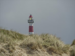 A red and white striped lighthouse behind grassy dunes under a cloudy sky, red and white lighthouse