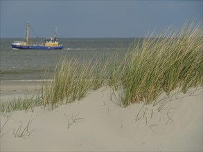 Sand dunes in the foreground with a boat on the sea and blue sky in the background, dune with dune
