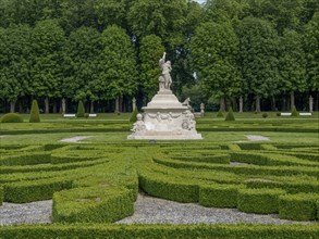 Extensive baroque garden with symmetrical hedge pattern and imposing sculptures, surrounded by