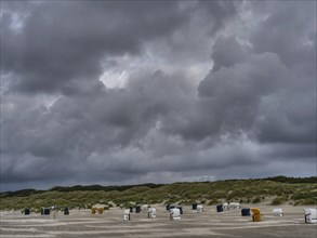 Deserted, stormy beach with dark clouds and dunes in the distance, colourful beach chairs on the