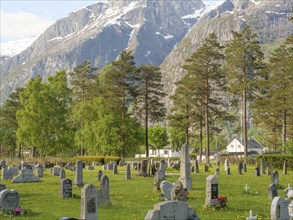 A cemetery in front of impressive mountains with numerous gravestones and trees in a peaceful and
