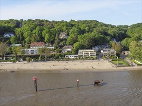 River bank with sandy beach, surrounded by houses and wooded hills in the sunshine, green bank on a