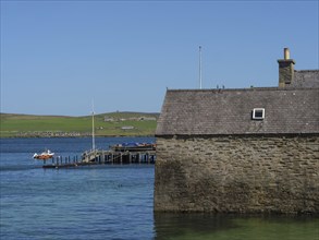 Stone building on the water with a pier and a small boat in the clear blue sea under a bright blue