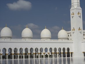 Side view of the mosque with white domes, golden decorations and columns under a blue sky,