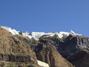White buildings high up on rocky cliffs under a clear blue sky, rocky island in the sea with white