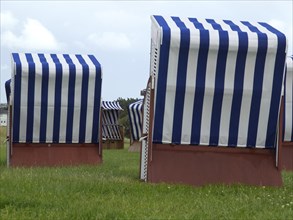 Some blue and white beach chairs on a green meadow under a cloudy sky, blue and white striped beach