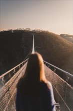 Woman looks into the distance at sunrise on the Geierlay suspension rope bridge in Moersdorf in