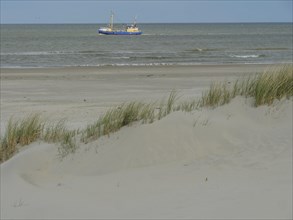 Blue boat in the sea behind sand dunes with reeds in calm weather, dunes by the sea with clouds in