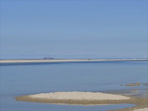 A sandy beach with a small island in the foreground, surrounded by blue water, wide sky on a lonely