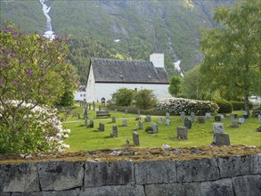 Cemetery with church and gravestones, surrounded by green landscape and high mountains, gravestones