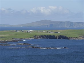 Peaceful coastal landscape with green hills and houses by the blue sea, green meadows by a deep