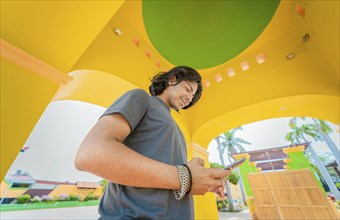 Low angle view of young man using cell phone outdoors. Smiling latin guy texting with cell phone in