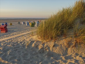 Sandy beach beach with colourful beach chairs and high dunes by the sea at dusk, sunset on a quiet