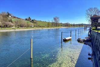 Clear river landscape with calm water, boat moorings and green hills in the background in bright