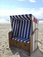 A single blue and white beach chair on the beach with the sea in the background and a cloudy sky,