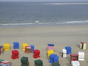 Various colourful beach chairs scattered on empty beach with calm sea in background, beach chairs