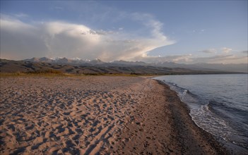 Sandy beach beach on the banks of Issyk Kul, with the peaks of the Tian Shan Mountains in the