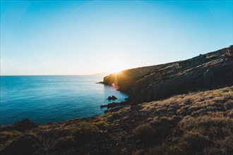 The sun sets behind steep coastal cliffs over the sea. Madeira Portugal