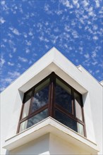 Facade of a white building with a large corner window and a cloudy blue sky