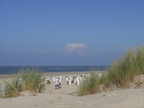 View of a quiet beach with dunes in the foreground and several empty beach chairs under a clear