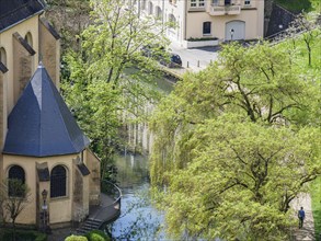 Church building next to a river, surrounded by green trees and other buildings in a spring-like