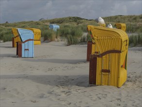 Colourful beach chairs and seagulls on the beach, surrounded by dunes and a cloudy sky, colourful