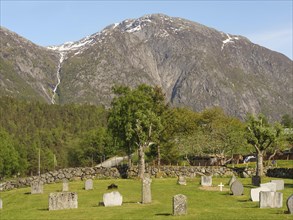 Cemetery on a large green area with mountains in the background on a sunny spring day, gravestones