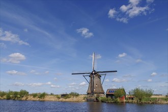 A windmill next to a small house under a clear sky with scattered clouds, many historic windmills