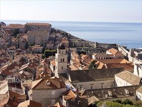 Panoramic view of a coastal town with historic stone buildings and red-tiled rooftops, overlooking
