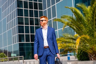 Cool businessman wearing suit and sunglasses carrying a laptop bag leaving the office after work