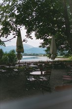View through parasols of a tranquil lake with mountains in the background. Lake Hopfensee, Bavaria
