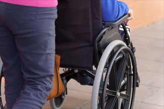 An unrecognizable woman pushing a wheelchair with a person sitting in it
