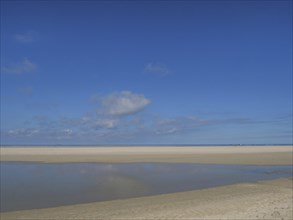 Spacious beach under a blue sky with few clouds and shallow water, wide sky on the lonely North Sea