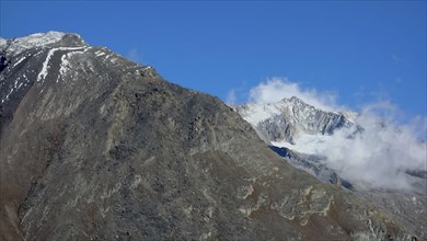 Steep rocky mountains with snow cover and clouds under a clear blue sky, snow on high mountains in