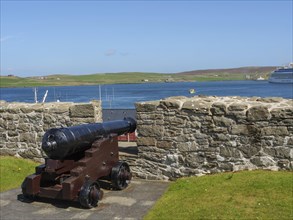 Historic cannon in front of a stone wall with a view of the sea, a ship and green hills, old