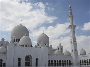 White mosque with several domes and a high minaret under a cloudy sky, large mosque with white