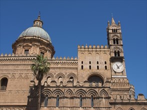 Historic cathedral with striking dome, clock and detailed towers, under a bright blue sky, two red