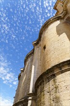Partial view of the facade of an old stone church with the cloudy blue sky in the background