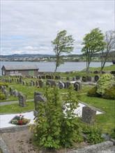 Cemetery with many gravestones, in the background a body of water, trees and a small house under a