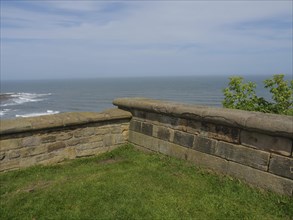 Stone wall overlooking the sea and the coast under a cloudy sky, surrounded by green nature, ruins