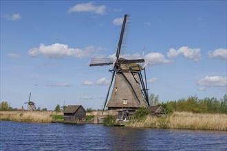 Windmill and buildings on a body of water under a blue sky with white clouds, many historic