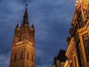 An illuminated Gothic church tower rises into the cloudy night sky of a historic city, historic